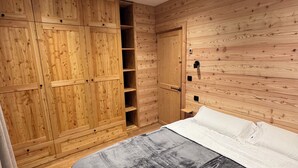 Een slaapkamer met houten paneelwanden, een bed met grijs dekbed en een ingebouwde houten kledingkast met verschillende vakken.