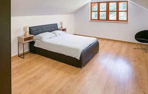 Une chambre à coucher comprenant un lit, des tables de chevet, une lampe, une chaise et une fenêtre donnant sur des arbres.