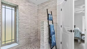 Een badkamer met een stenen muur, een raam met een gezandstraald glaspaneel en een handdoekrek met twee handdoeken.