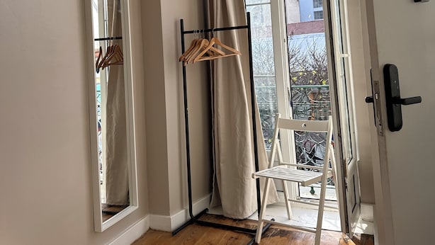 A room with a wooden floor, a bed, a mirror, a coat rack, a chair, and a window with curtains. - Bohemian Stay Central Lisbon Rooms (Lisbon)