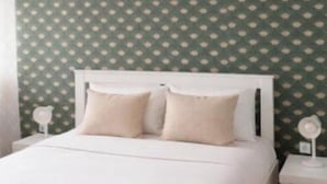 A bedroom with a white bed, green patterned wallpaper, and a wooden floor. - Bohemian Stay Central Lisbon Rooms (Lisbon)