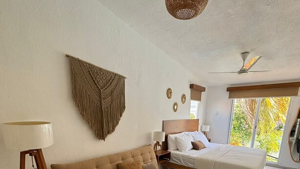 A modern bedroom with a sofa, bed, and a small table with a plant. - Comfortable and spacious room w/alberca (Cancún)
