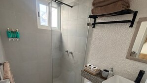 A bathroom with a glass-enclosed shower, a toilet, a sink, and a towel rack. - Comfortable and spacious room w/alberca (Cancún)