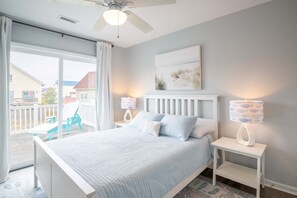 Slaapkamer met een bed, twee nachtkastjes, een plafondventilator, een raam met gordijnen en uitzicht op buiten.