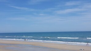 Een strand met heldere lucht, rustige zee en enkele mensen die wandelen.