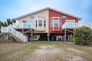 A two-story building with a red and beige facade, a covered front porch, and a small balcony on the upper floor. - Evy's Wave - Sound View - Dogs Allowed (North Topsail Beach)