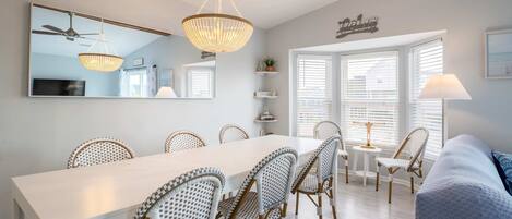 A dining area with a white table, wicker chairs, a chandelier, and a ceiling fan.
