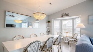 A dining area with a white table, wicker chairs, a chandelier, and a ceiling fan. - Great Catch - Double Duplex - Dogs Allowed - Wraparound Deck (North Topsail Beach)