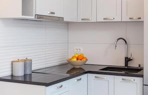 A modern kitchen with white cabinets, a black countertop, a stainless steel sink, and a bowl of fruit. - Lovely apartment in Sutivan with house sea view (Sutivan)