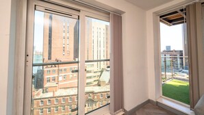 Una habitación con ventanas amplias, vistas a edificios y un balcón con césped.