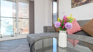 Una sala moderna con una mesa de centro de vidrio curvo, un sofá gris y un jarrón con flores.