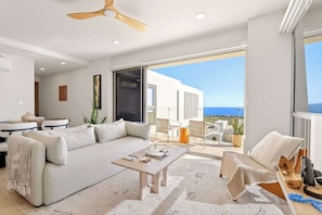 Un salon moderne avec un canapé, une table basse et une vue sur la mer grâce à de grandes fenêtres.