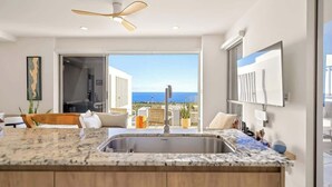 Une cuisine moderne dotée d’un grand îlot central, d’un ventilateur de plafond et offrant une vue sur l’océan.
