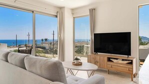 Una sala de estar moderna con un televisor de pantalla plana grande, un sofá, una mesa de centro y vistas al mar.