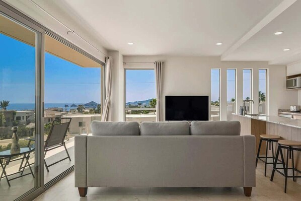 Een moderne woonkamer met een bank, een televisie en een balkon met uitzicht op zee.