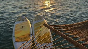 Una hamaca con dos tablas de surf apoyadas, con vista al mar tranquilo al atardecer.