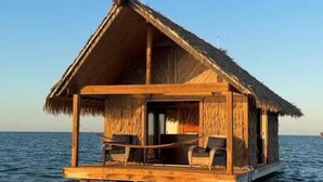 Una estructura de madera flotante con techo de paja, un porche cubierto y asientos.