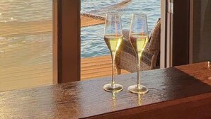 Una habitación con vistas al mar, dos copas de vino blanco sobre una mesa de madera y una silla de mimbre.