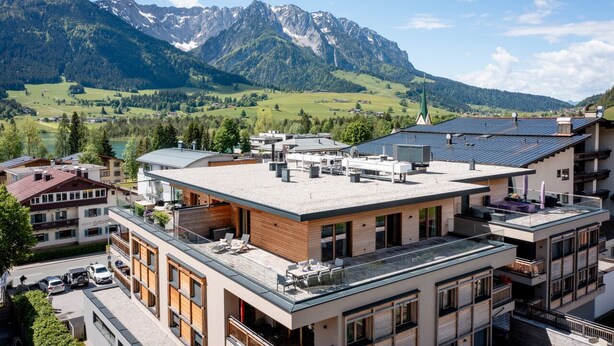 Um hotel moderno com terraço no telhado, rodeado por uma paisagem montanhosa.