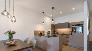 Uma cozinha moderna com ilha central, iluminação pendente e área de refeições com mesa e cadeiras de madeira.