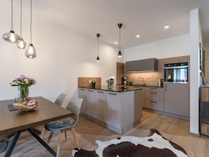 A modern kitchen with a central island, pendant lighting, and a dining area with a wooden table and chairs. - Get out of everyday life and into the vacation feeling! (Walchsee)