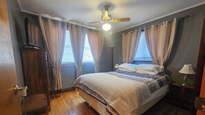 Une chambre à coucher avec un lit, des rideaux, un ventilateur de plafond et une table de chevet avec une lampe.