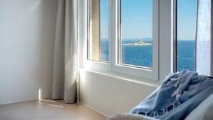 Habitación con un ventanal grande que da a una vista costera, con un faro y un mar tranquilo.