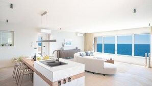 Un espacio habitable moderno con isla de cocina, zona de estar y un amplio ventanal con vistas al mar.