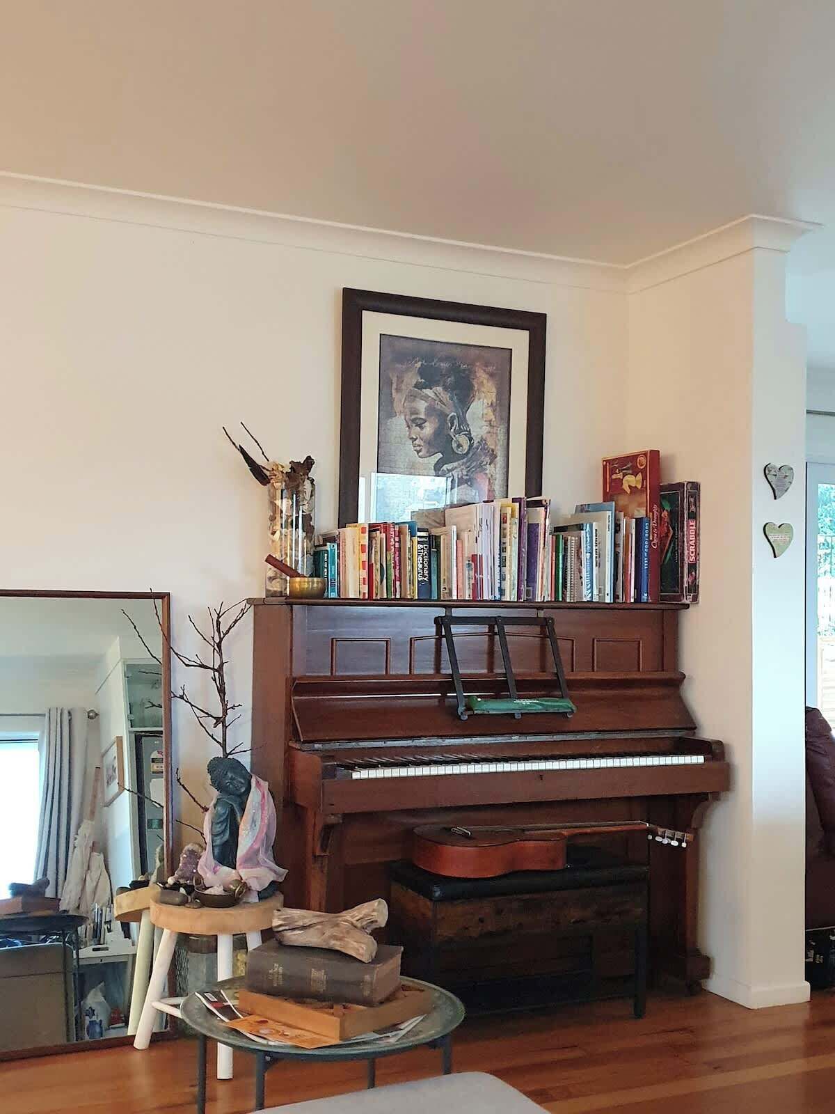 A living room with a piano, a bookshelf, a small table with books, and a framed picture on the wall.