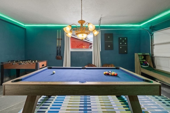 Une table de billard avec des billes, une table de baby-foot et un lustre.