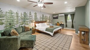 Un dormitorio con cama, sofá, ventilador de techo, alfombra y una pared con un mural de un bosque.