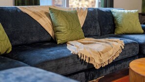 Un sofá azul oscuro con una manta color beige y almohadas verdes.