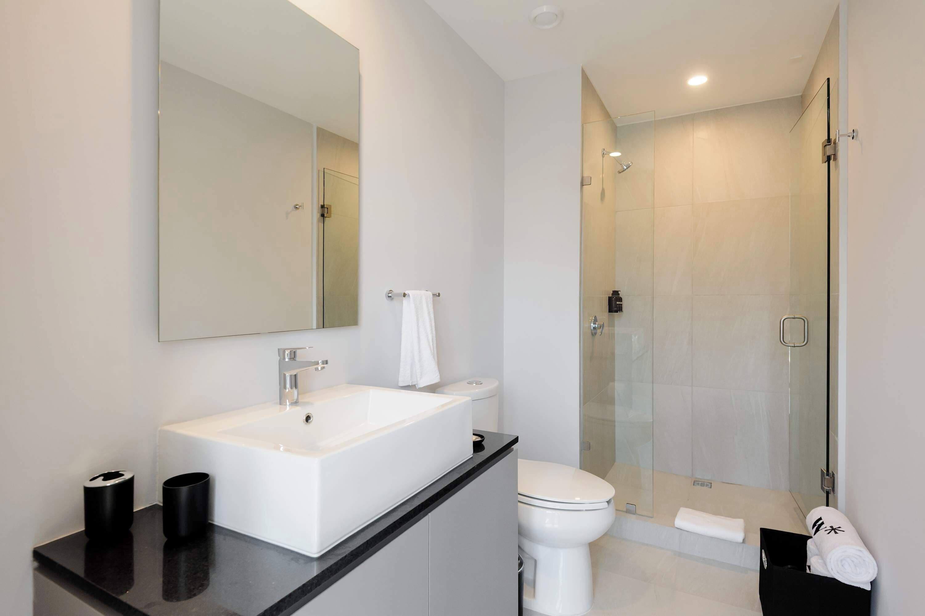 A modern bathroom with a large mirror, white sink, and glass-enclosed shower.
