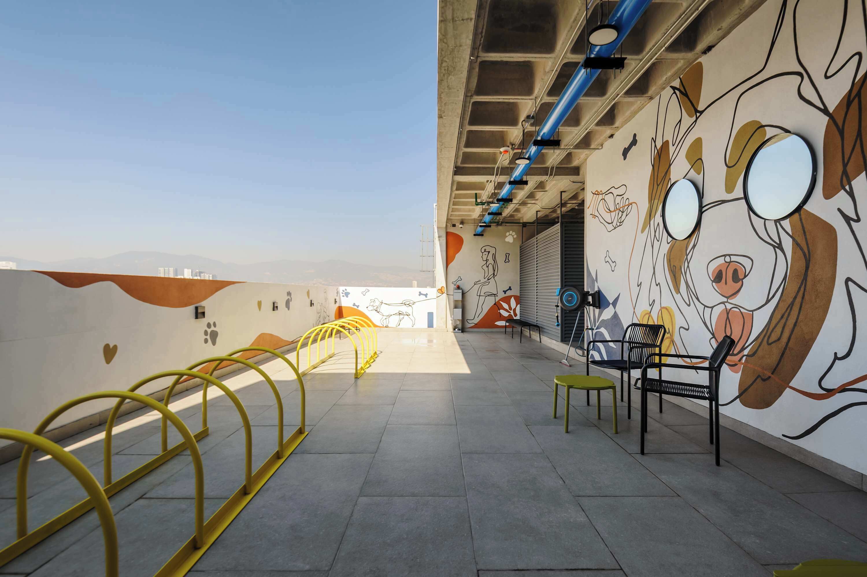 Un pasillo interior con un mural, barandas amarillas y zonas de estar.
