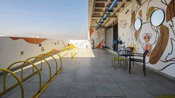 Un pasillo interior con un mural, barandas amarillas y zonas de estar.