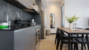 Een moderne keuken met een centraal eiland, roestvrijstalen apparatuur en een eethoek met een houten tafel en zwarte stoelen.