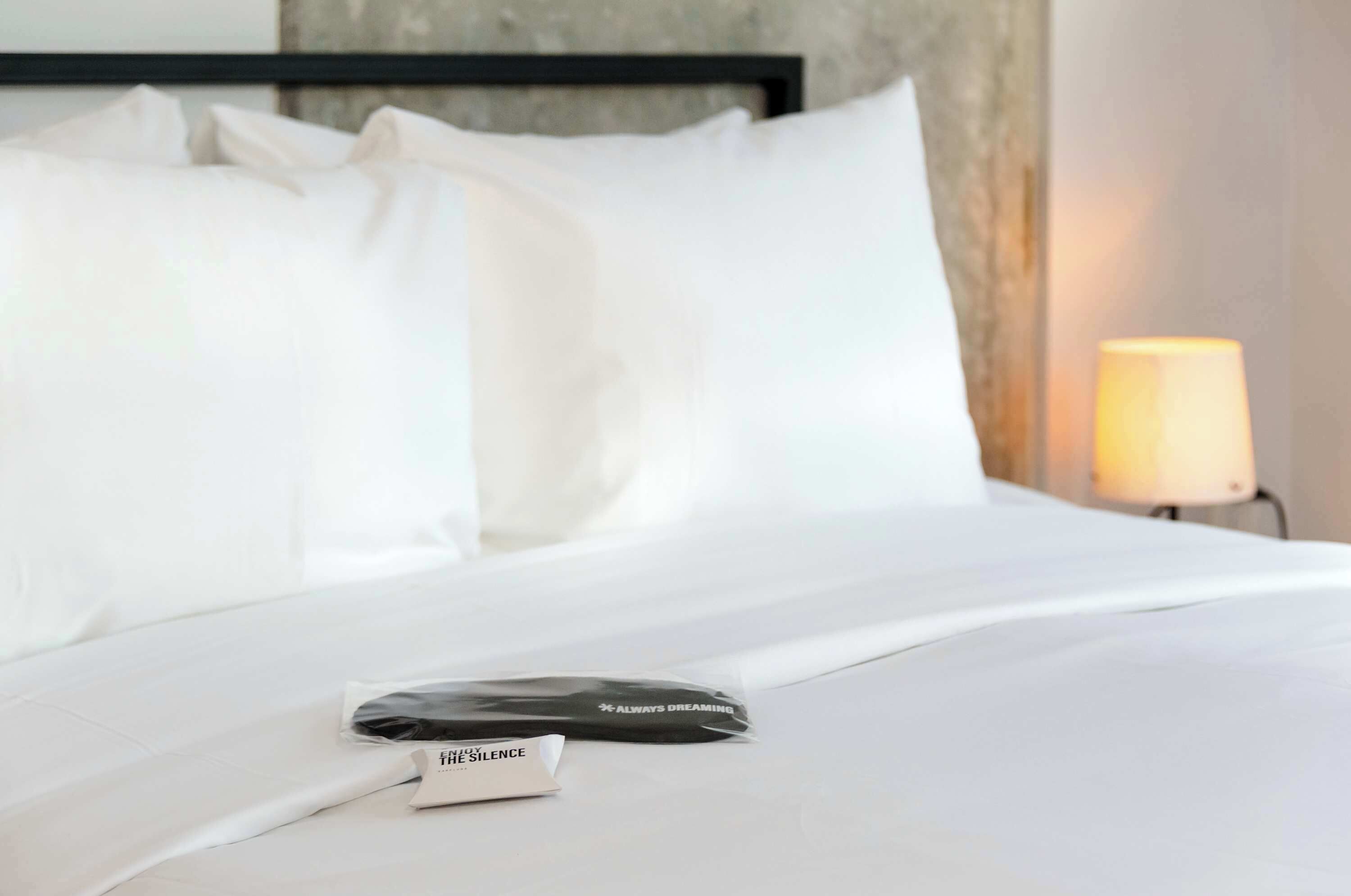 A neatly made bed with white linens, a pillow, and a black object on the bed.