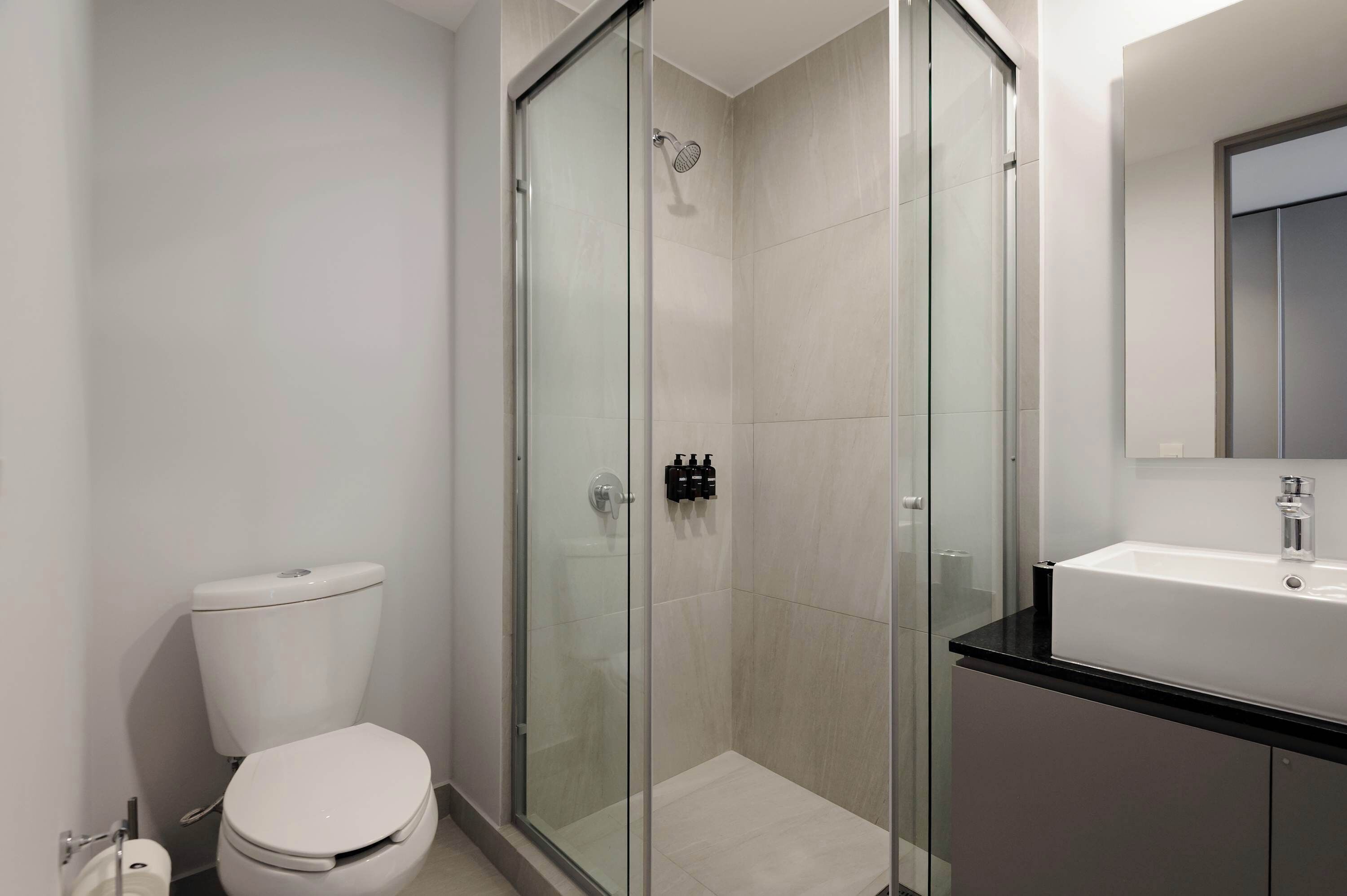 Une salle de bain moderne avec une douche à parois de verre, des toilettes blanches et un lavabo doté d’un plan de travail noir.