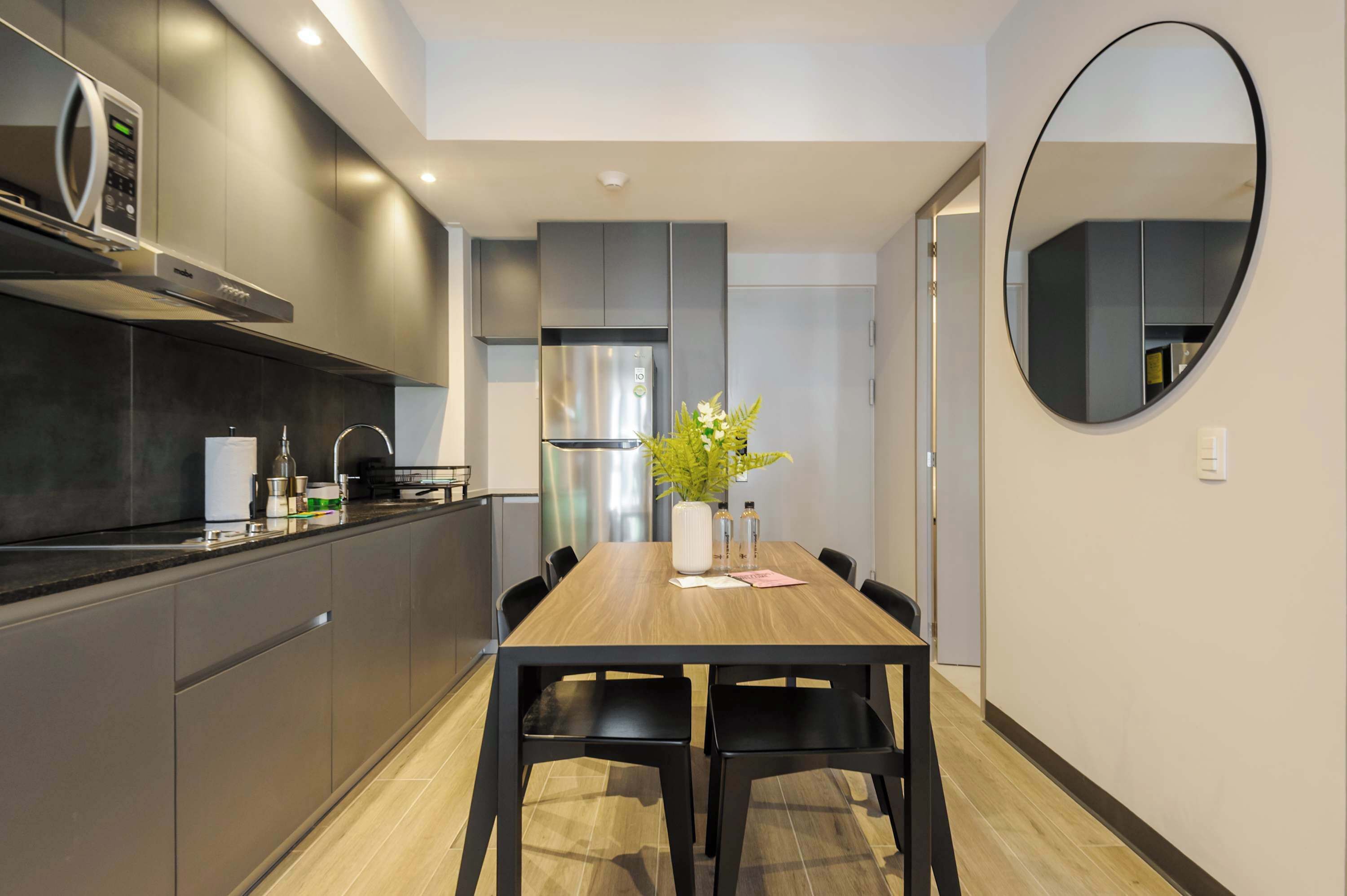 Une cuisine moderne avec des meubles de couleur sombre, un réfrigérateur en acier inoxydable et une table à manger en bois, assortie de chaises noires.