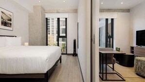 Een moderne hotelkamer met een groot bed, een bureau, een stoel, een televisie en een uitzicht op de stad door grote ramen.
