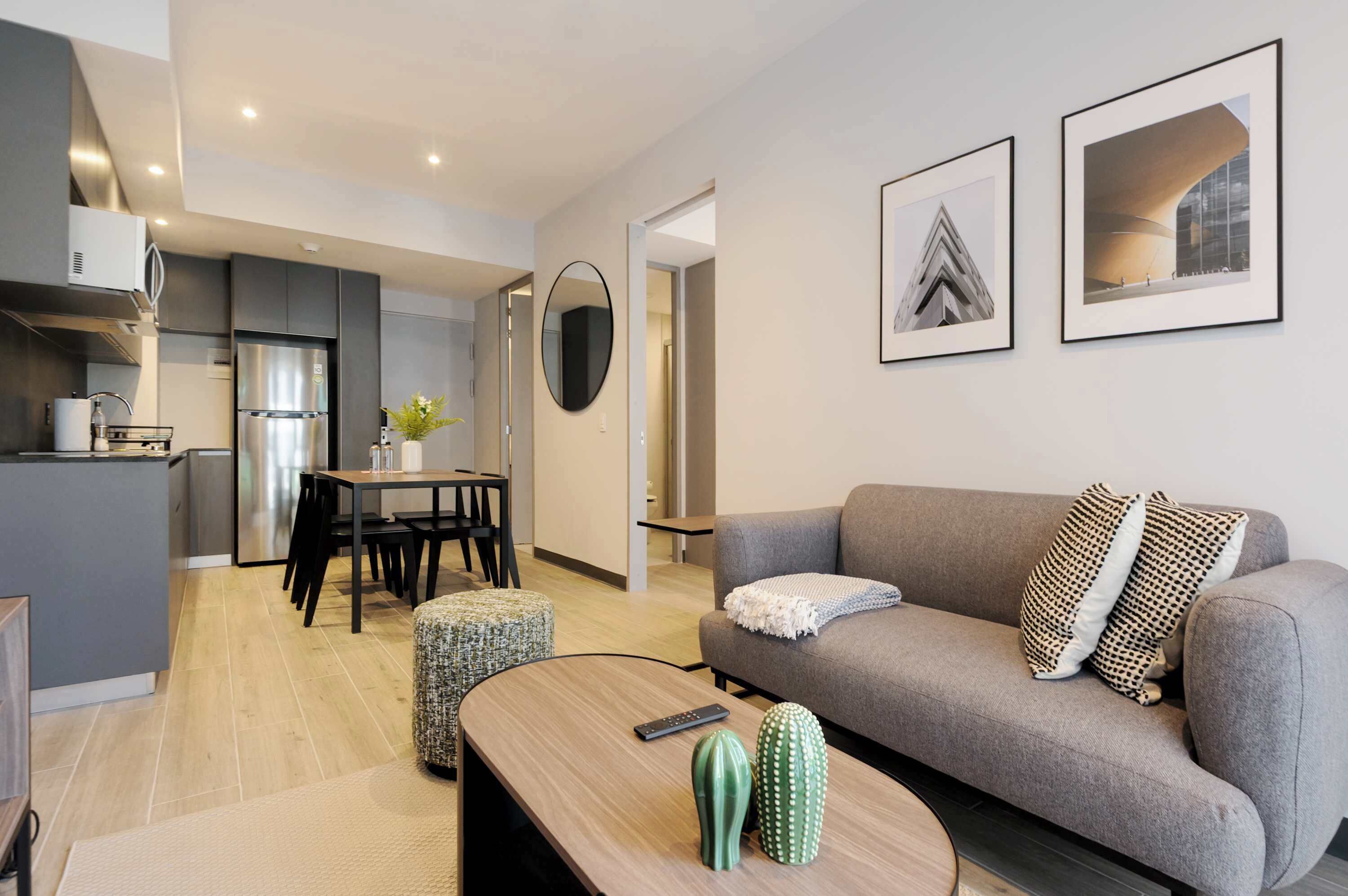 Un appartement moderne avec un canapé gris, un coin repas, une cuisine et deux tableaux encadrés accrochés au mur.