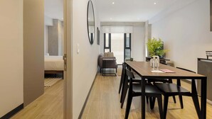 Moderni hotellihuone, jossa on puinen ruokapöytä, mustat tuolit, sohva ja suuri peili.