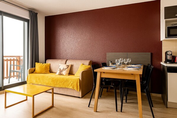 A modern living room with a sofa, a dining table set for two, and a kitchen area with a coffee machine. - T3 in the heart of Valberg, close to the slopes, heart of the resort, heated swimming pool (Péone)
