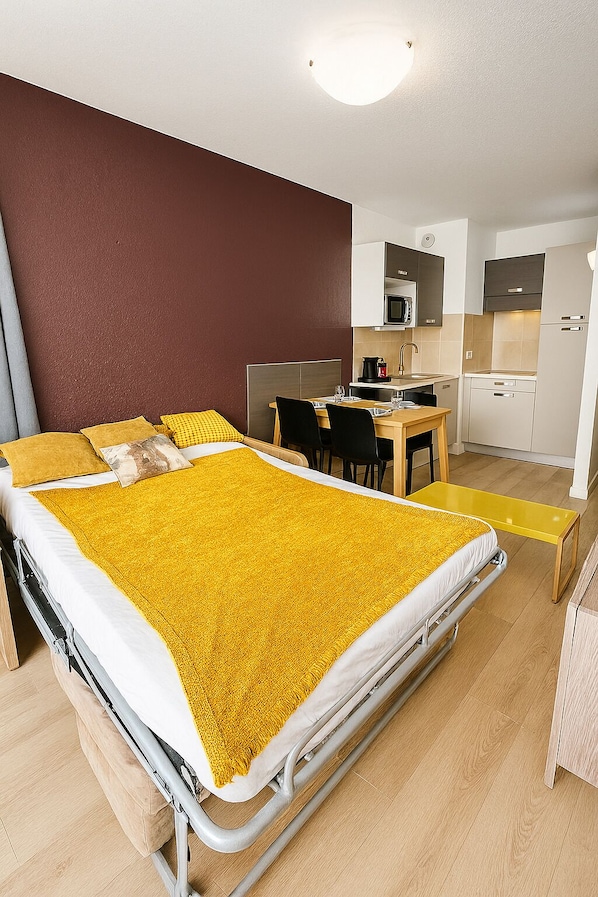 Une chambre d’hôtel de taille réduite, comprenant un lit, une petite table à manger et une kitchenette.