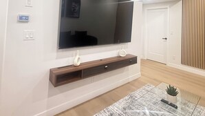 Un salon moderne avec un grand téléviseur à écran plat fixé au mur, un plancher en bois et un tapis à motifs.