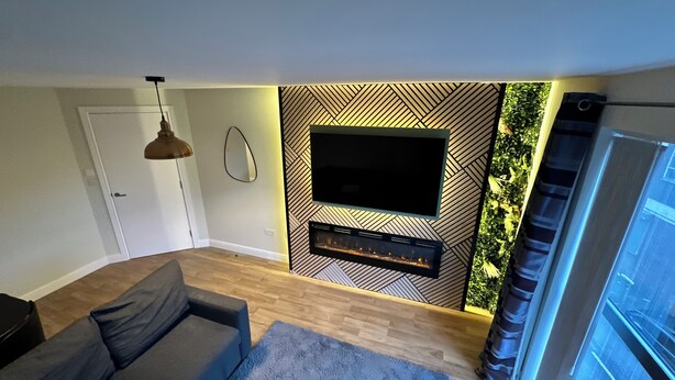 Una sala de estar moderna con un televisor de pantalla plana montado en una pared con diseño geométrico, un sofá gris y una alfombra pequeña.