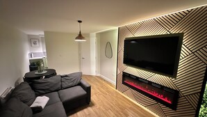 Una sala de estar moderna con un sofá seccional, un televisor de pantalla plana montado en una pared con diseño geométrico y una chimenea empotrada.
