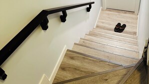 A staircase with a black handrail and wooden steps. - Modern 2 Bedroom Suite (Airdrie)