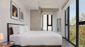 Un dormitorio moderno con una cama grande, una mesita de noche y vistas al exterior a través de amplios ventanales.