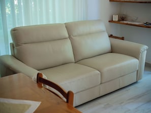 A beige leather sofa in a room with a wooden table and a shelf with decorative items.
